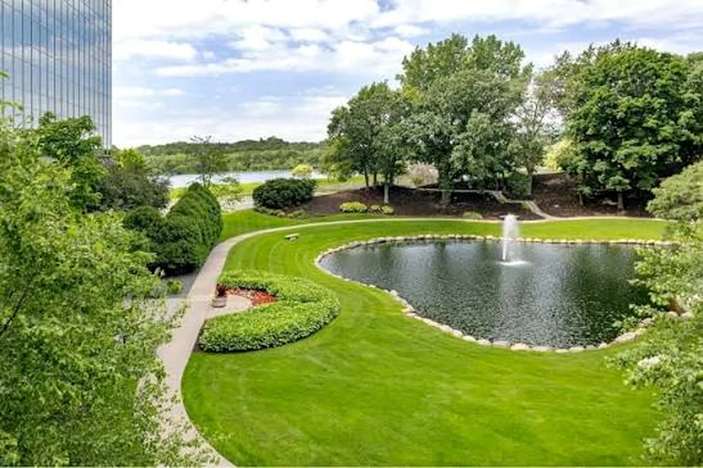 Commercial campus landscape with maintained lawn, trees, paths, and a pond