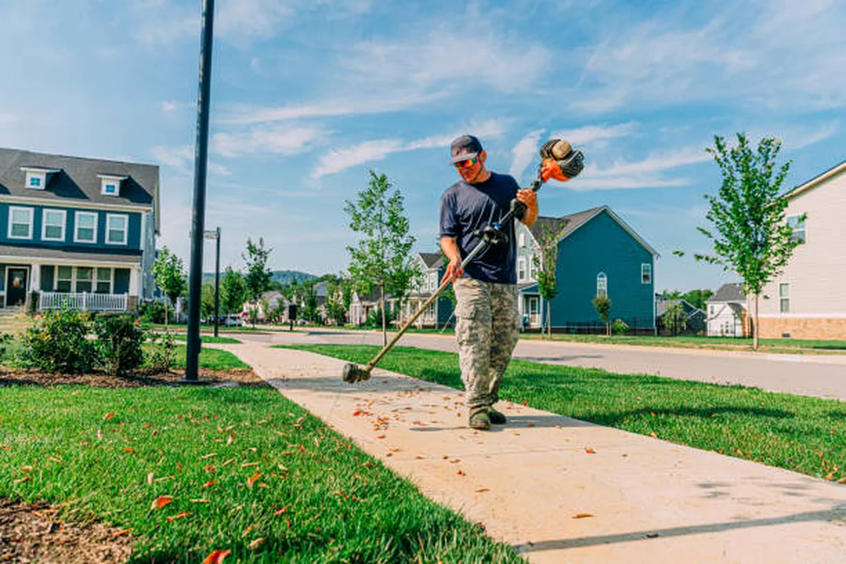 Landscape maintenance worker trimming grass along a neighborhood walkway